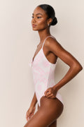 Woman wearing a pink swimsuit with thin straps against a beige background