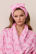 Woman wearing a pink robe and headband with a bow on a beige background