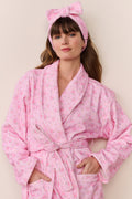 Woman wearing a pink robe and matching headband with a bow on a beige background