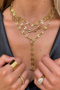 Close-up of a person wearing a gold chain necklace with multiple rings on fingers.