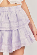 Woman wears mini purple tie-dye ruffle skirt against beige background