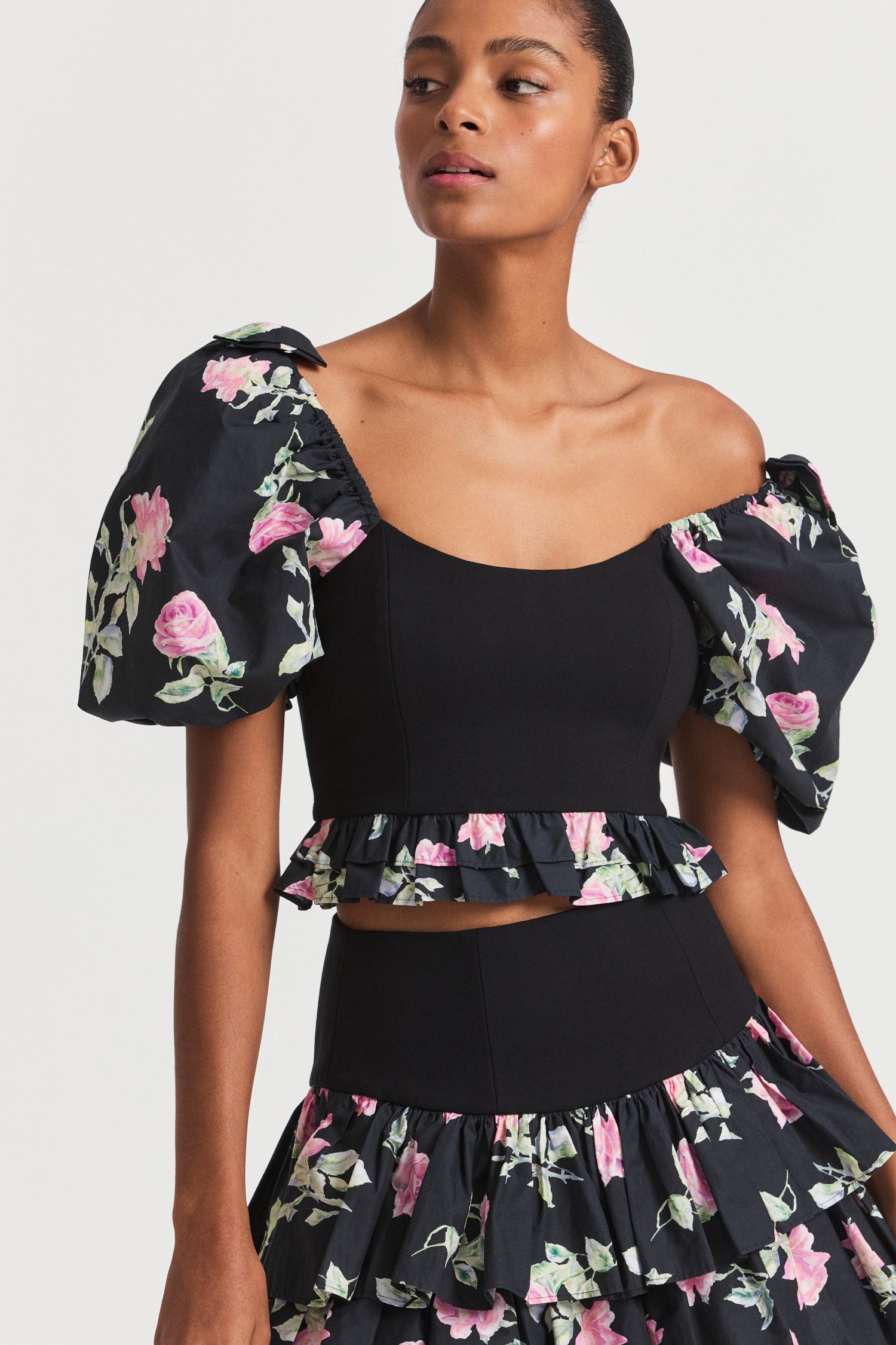 Black floral crop top with puff sleeves, a stretchy bodice and ruffle peplum detailing lines the hem of the top.