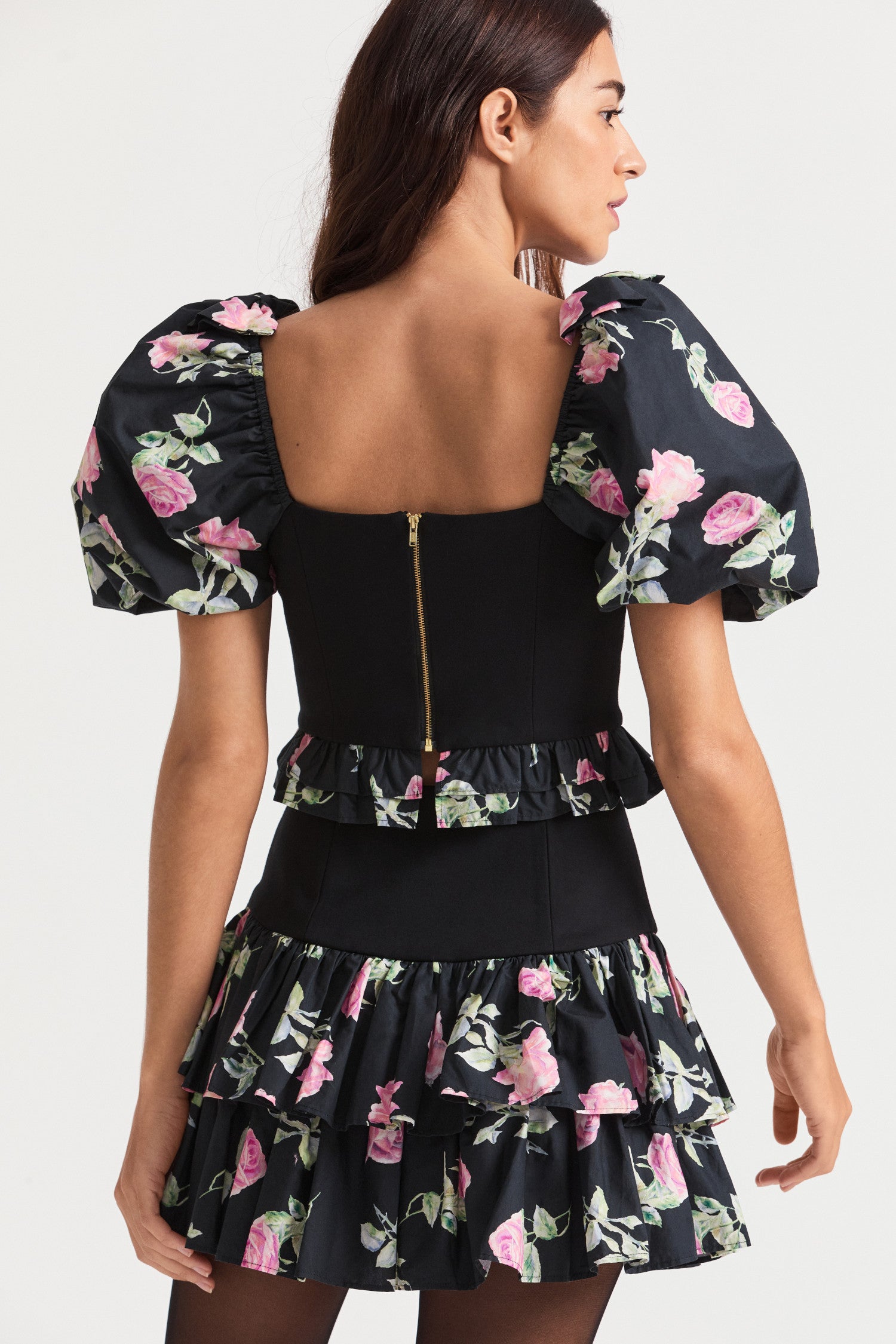 Black floral crop top with puff sleeves, a stretchy bodice and ruffle peplum detailing lines the hem of the top.