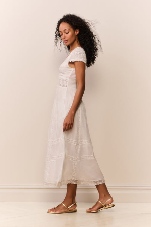 Woman wearing a white dress standing against a plain background