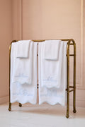 White towels with embroidery on a brass towel rack against a beige wall.