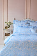 Blue floral bedding set on a bed with a decorative headboard and side table.