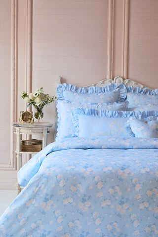 Blue floral bedding set on a bed with a decorative headboard and side table.