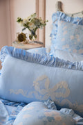 Blue baby crib set with floral patterns and ruffles, placed against a neutral wall.