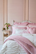 Pink and white bedding set on a bed with a decorative headboard and side table.