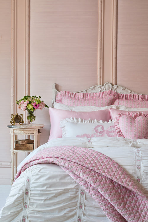 Pink and white bedding set on a bed with a decorative headboard and side table.