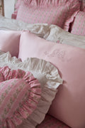 Pink and white ruffled pillows with floral patterns on a bed.