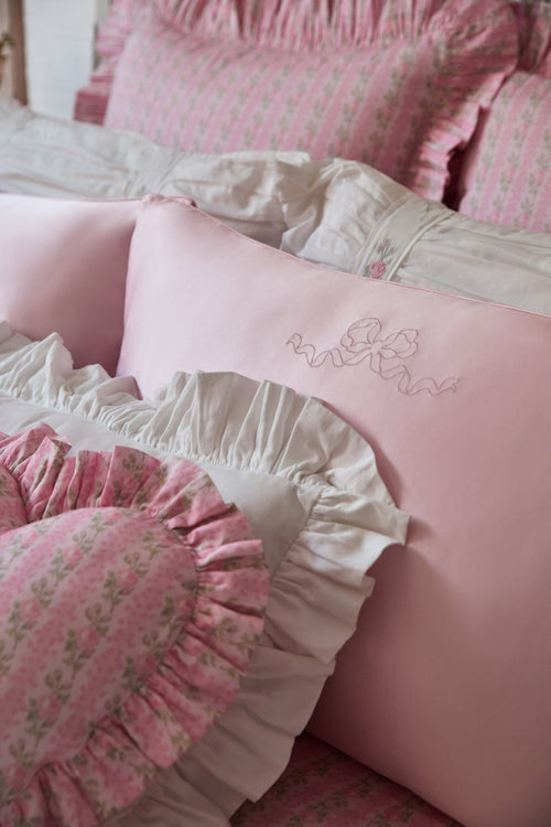 Pink and white ruffled pillows with floral patterns on a bed.