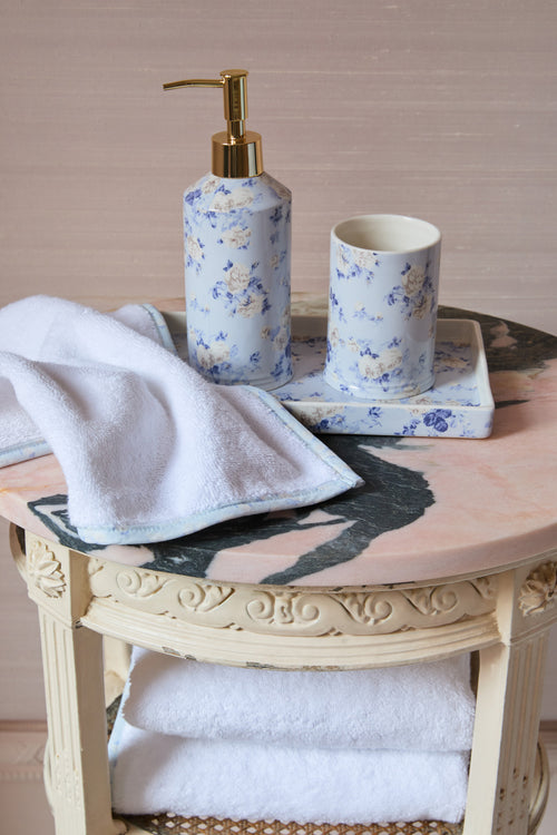 Bathroom set with floral soap dispenser, cup, and towel on a decorative table.