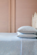 Light blue sheets and pillows with white polka dots on a bed against a pink wall.