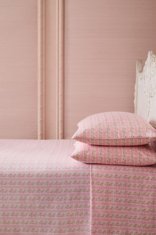 Pink floral bedspread and pillows on a bed against a pink wall.