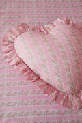 Pink heart-shaped pillow with ruffled edge on a matching pink floral fabric background