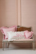Pink and white pillows on a wooden bench against a pink wall.