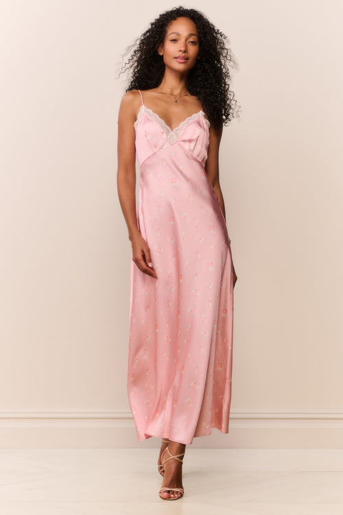 Woman wearing a pink satin white lace trim slip dress against a plain background