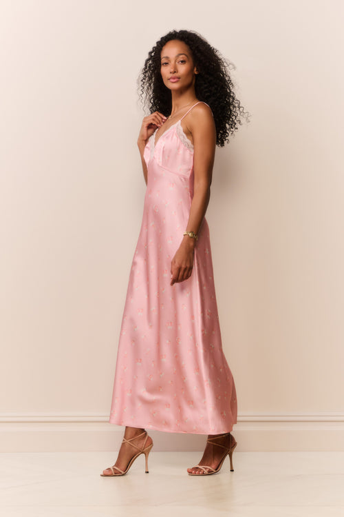 Woman wearing a pink satin white lace trim slip dress against a plain background