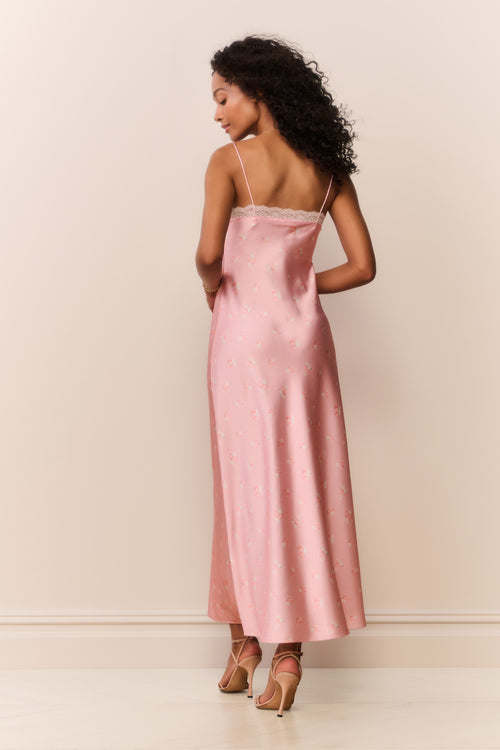 Woman wearing a pink satin white lace trim slip dress against a plain background