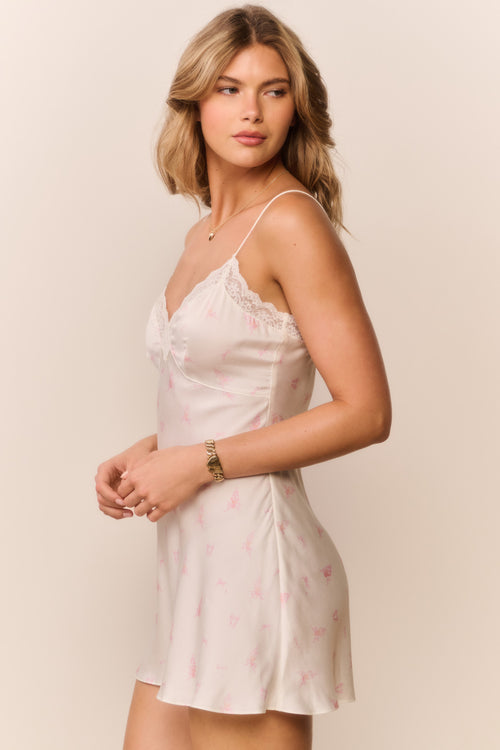 Woman wearing a white lace-trimmed and small floral print slip dress against a beige background