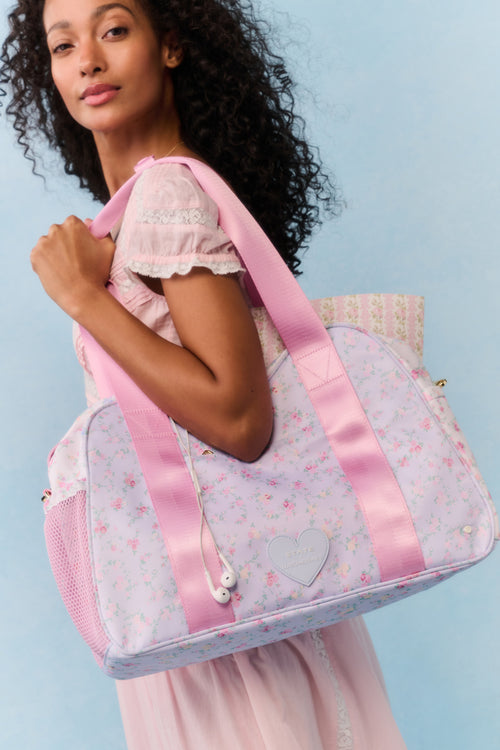Woman holding a pink and white floral-patterned bag against a light blue background