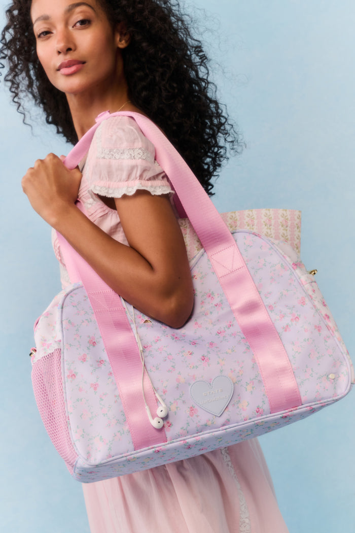 Woman holding a pink and white floral-patterned bag against a light blue background