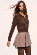 Brown cropped cable-knit cardigan featuring black bow details at the shoulders, black ribbon laced vertically down the front, and buttoned knit placket