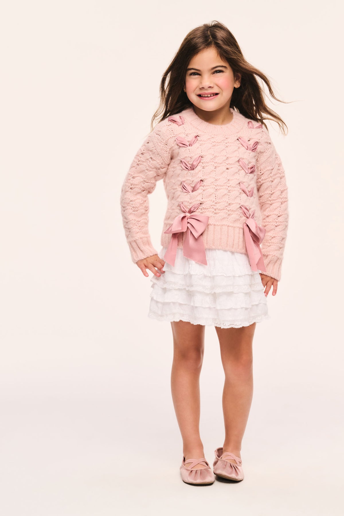 Girls' pink cable-knit cardigan front view with large ribbon threaded through and bow at hem