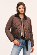 Front view of brown quilted jacket with dark brown corduroy collar and corduroy trim, snap button front, and front pockets with velvet bow trim, and model with her hand in her pocket