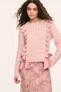 Pink textured knit pullover with crew neckline and ribbons laced down the front and bows at the hem, front view