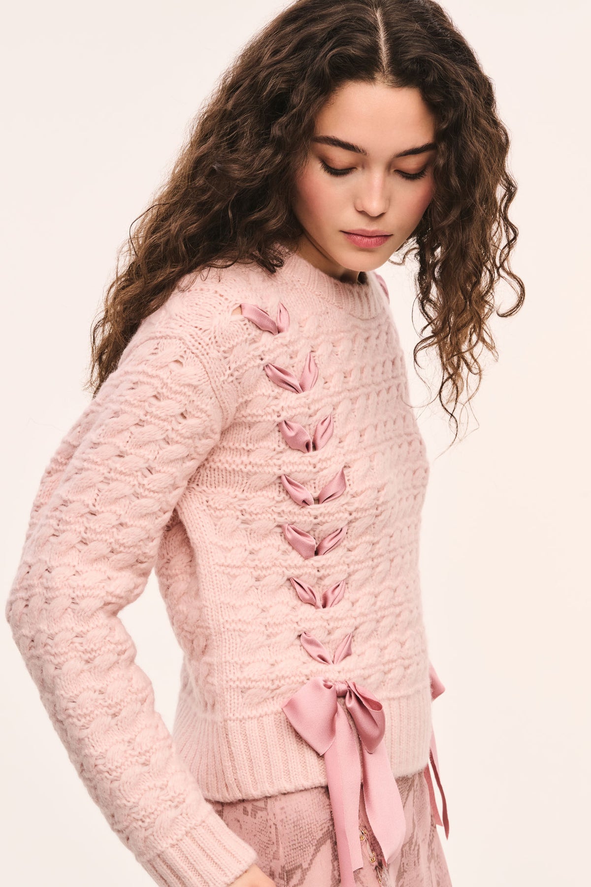 Pink textured knit pullover with crew neckline and ribbons laced down the front and bows at the hem, side view