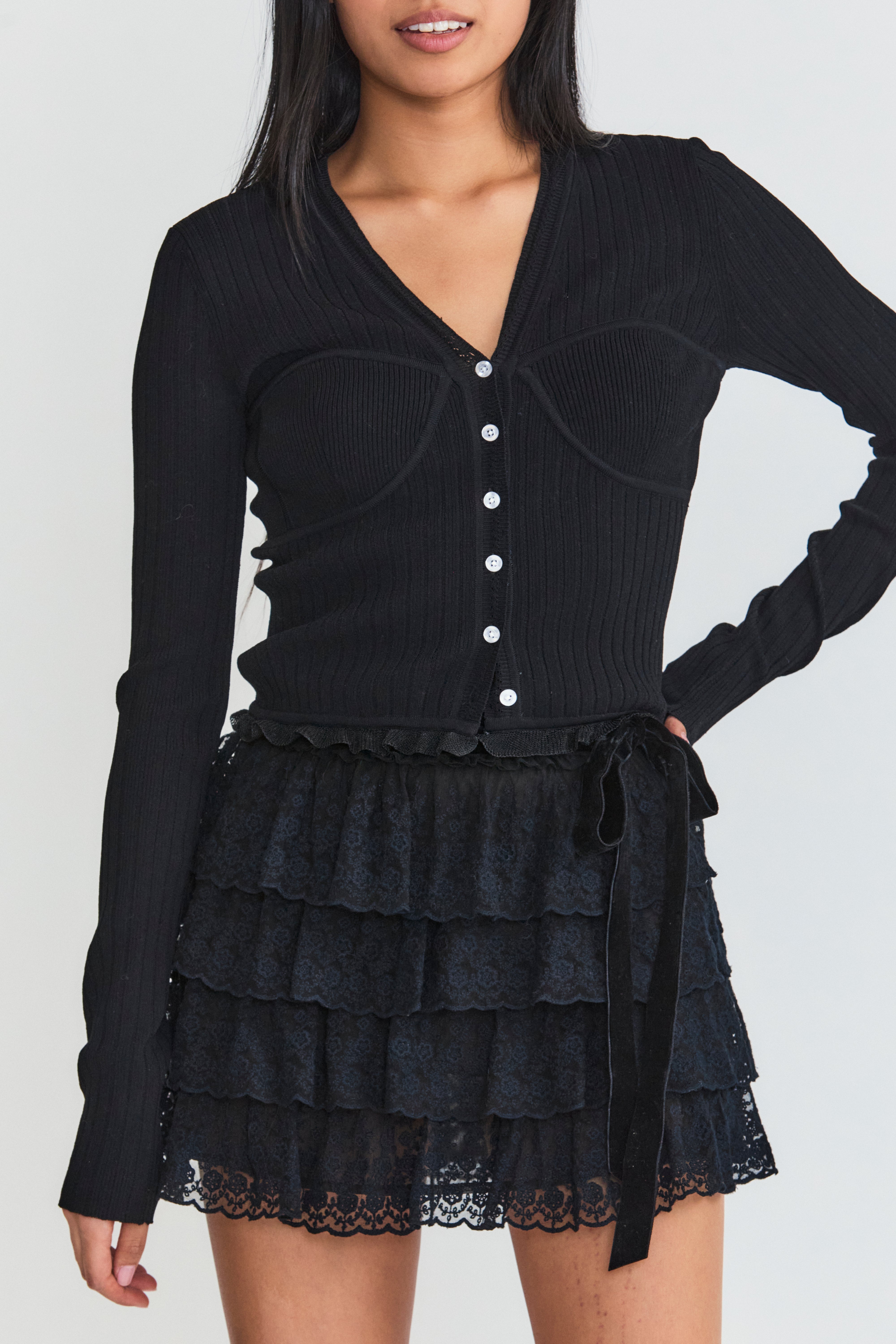 Model wearing black v-neck cardigan with ruffle detail at hem and button up closure.