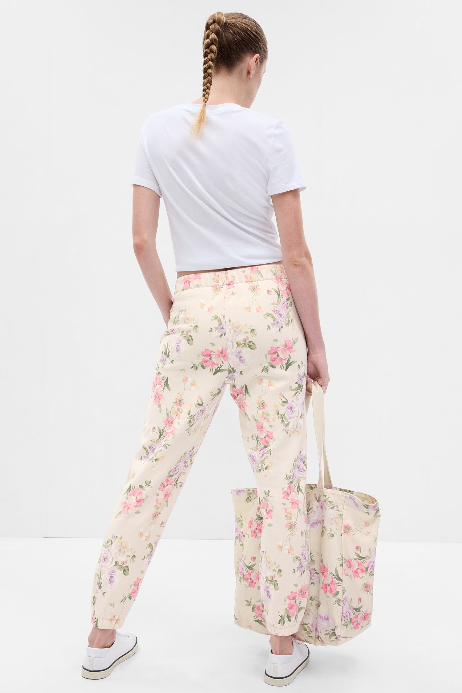 Back image of model wearing cream floral joggers with pink, purple, and green floral print
