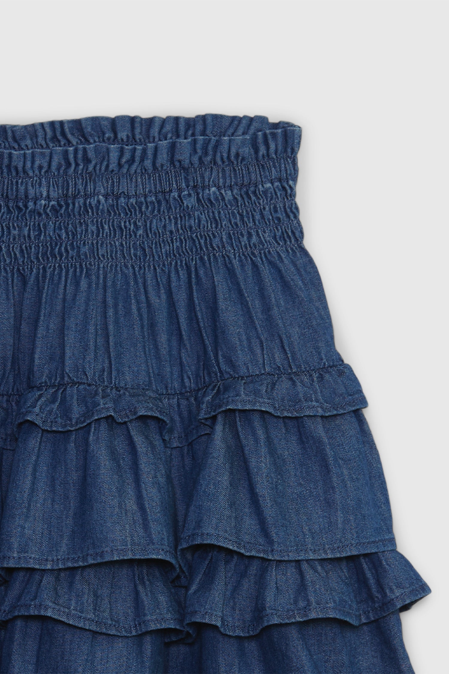 Close up image detailing waist on kids denim ruffle mini skirt with smocked waist and ruffle skirt