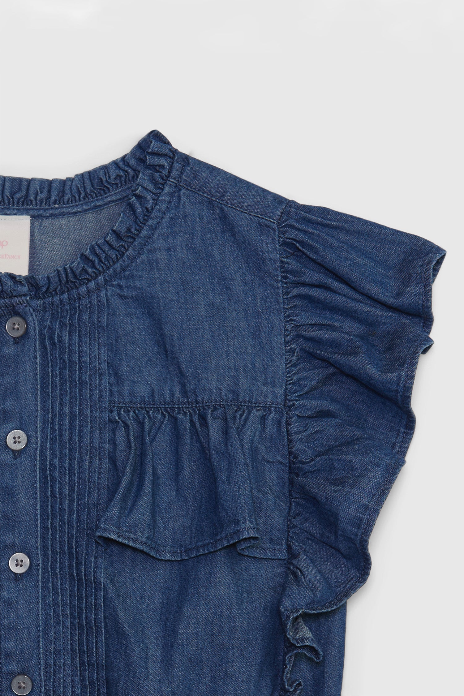 Close up image detailing kids denim ruffle top with buttons at front and ruffled short sleeves.