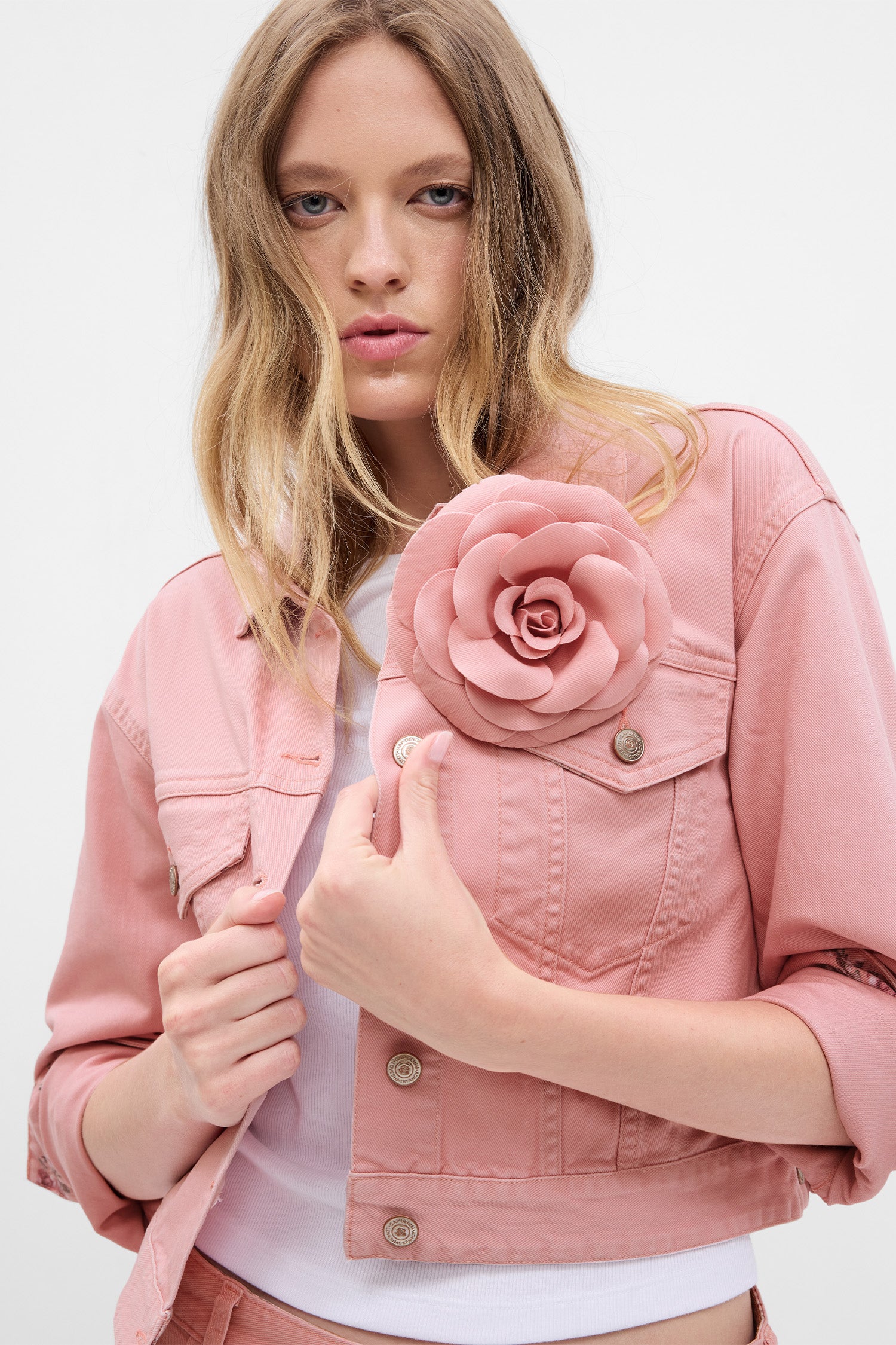 Model wearing pink denim jacket with rosette on chest