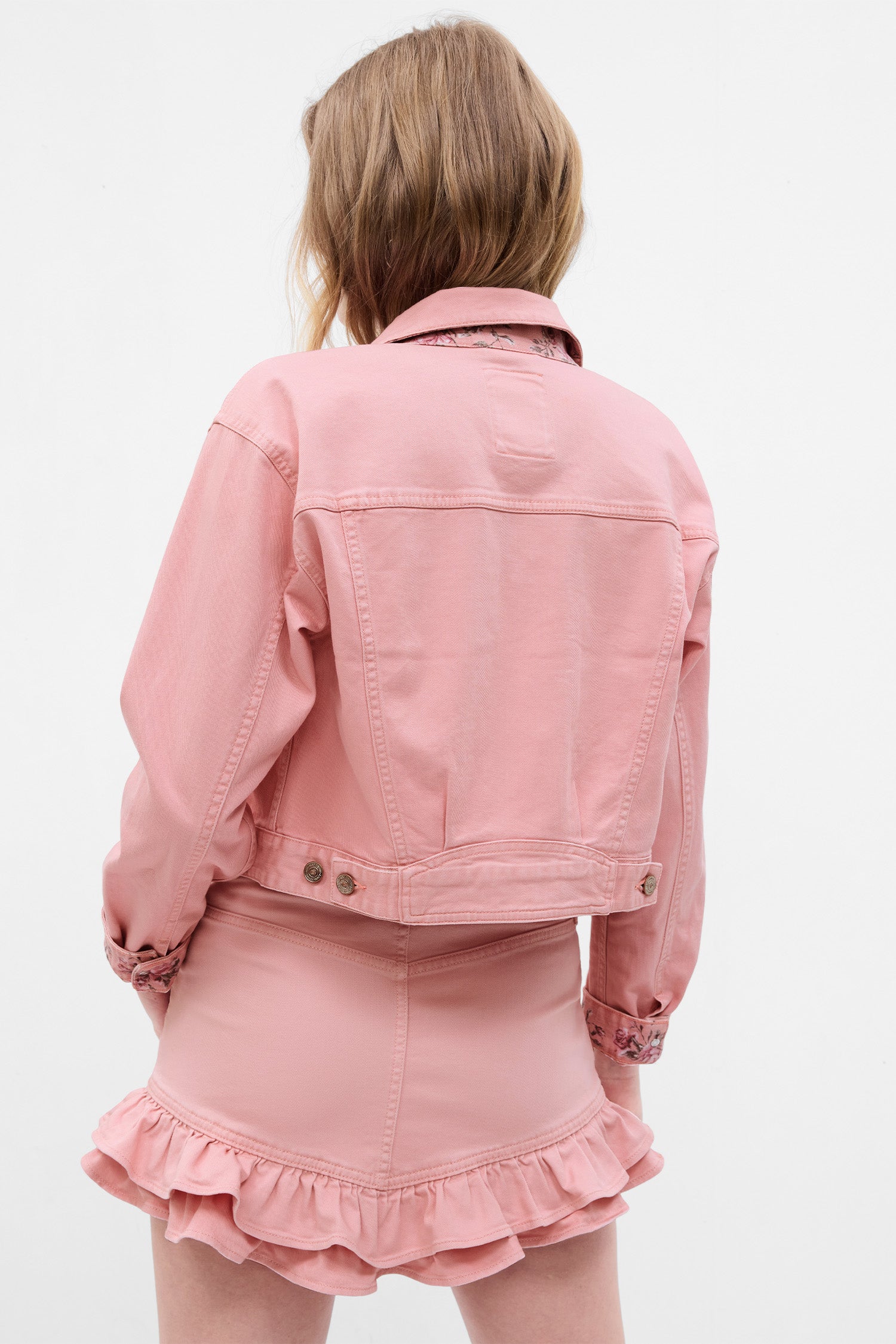 Back image of model wearing pink denim jacket with rosette on chest