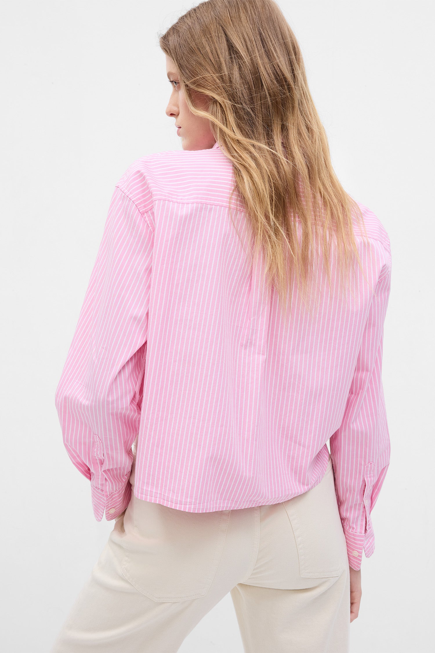 Back image of model wearing pink and white striped crop button up shirt with rosette detail on shoulder