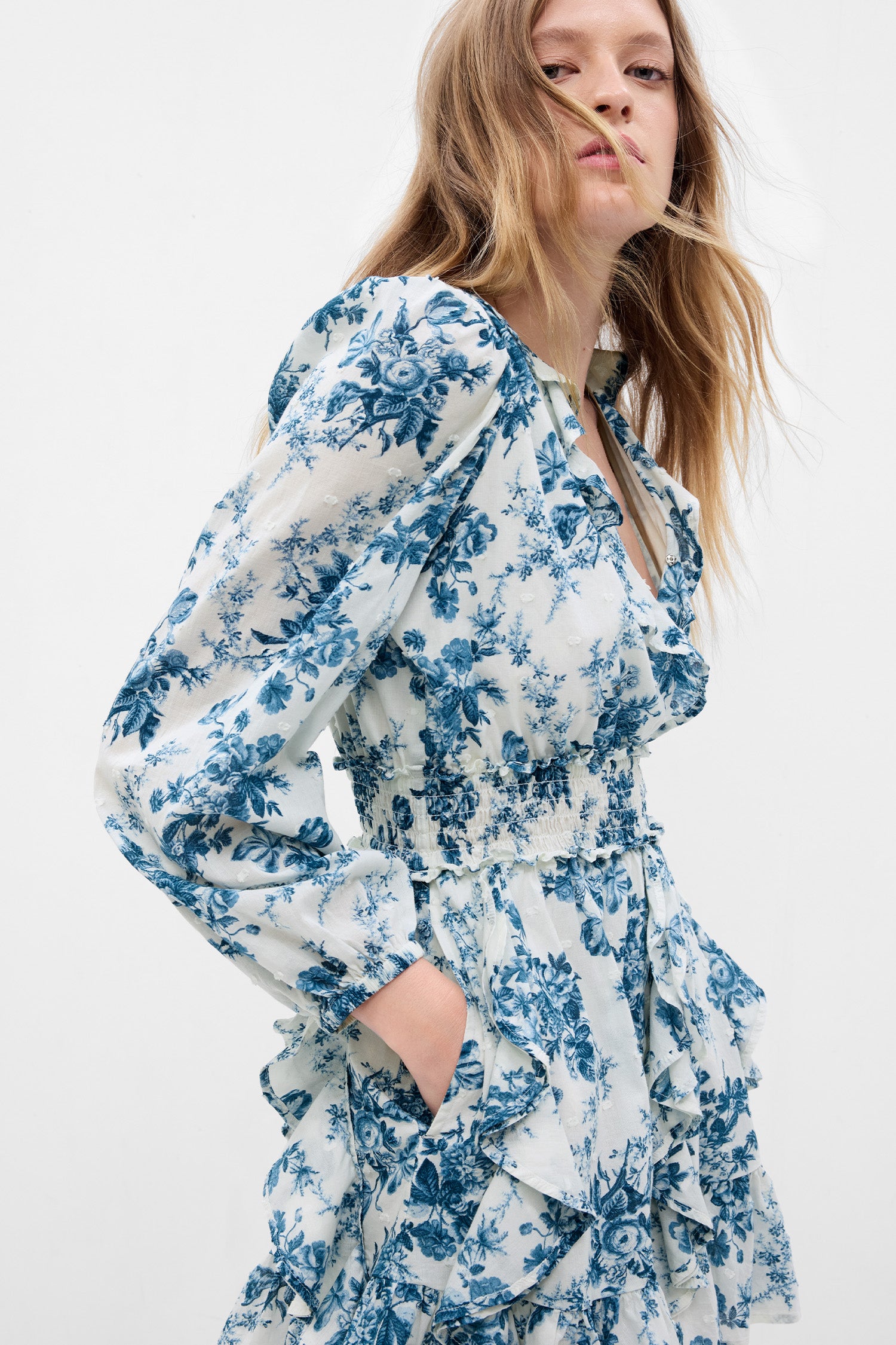 Model wearing white and blue floral mini dress with puff long sleeves, ruffled hem, and smocked waist