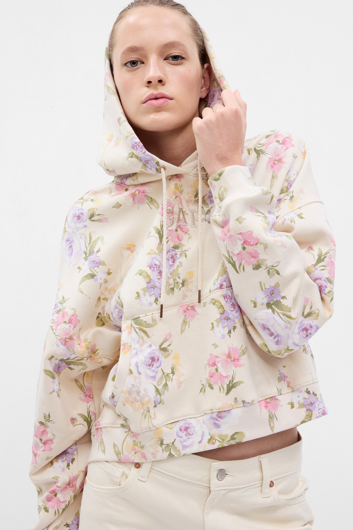 Model wearing cream floral hoodie with GAP arch logo on chest and pink, purple, and green floral print