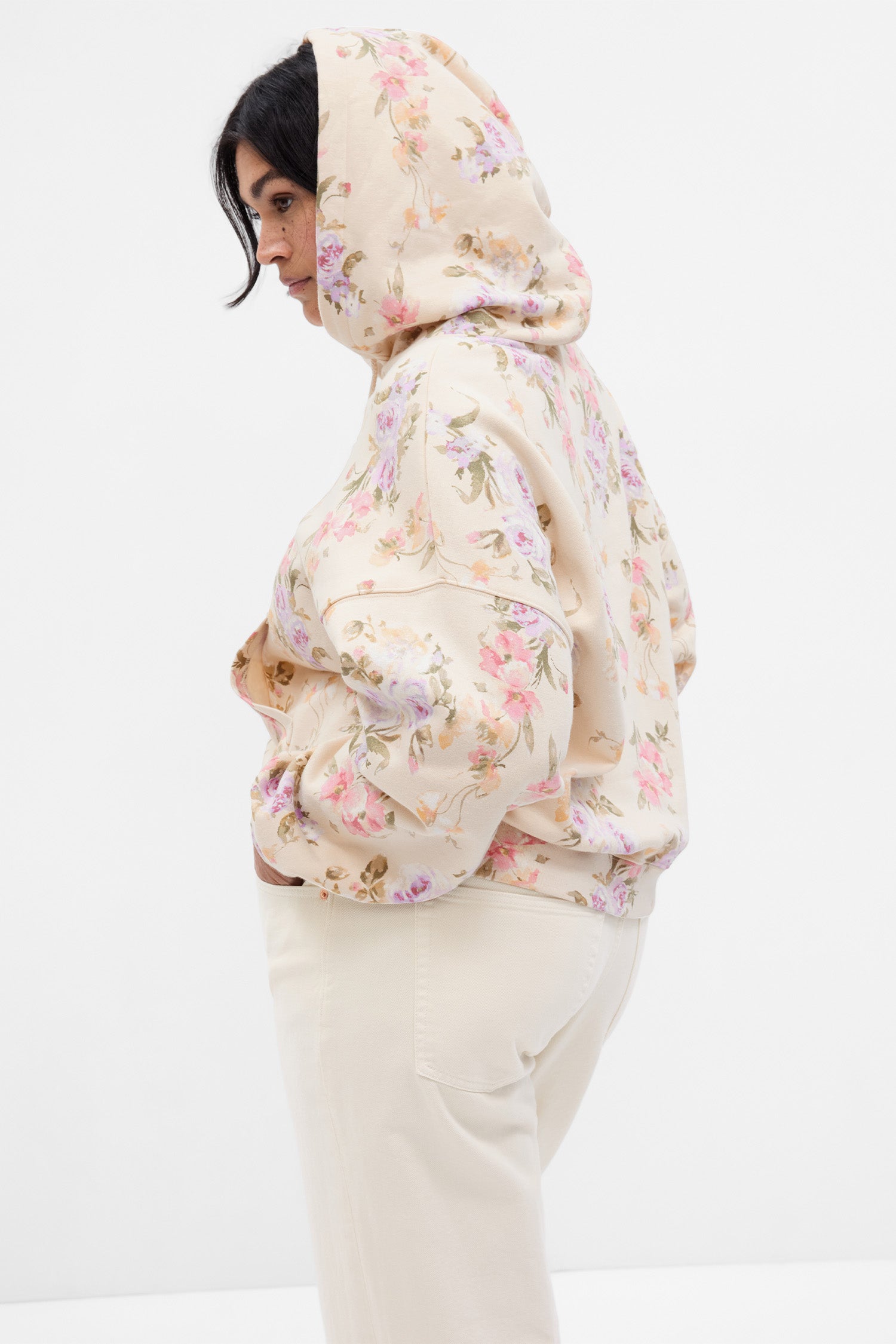 Side image of model wearing cream floral hoodie with GAP arch logo on chest and pink, purple, and green floral print