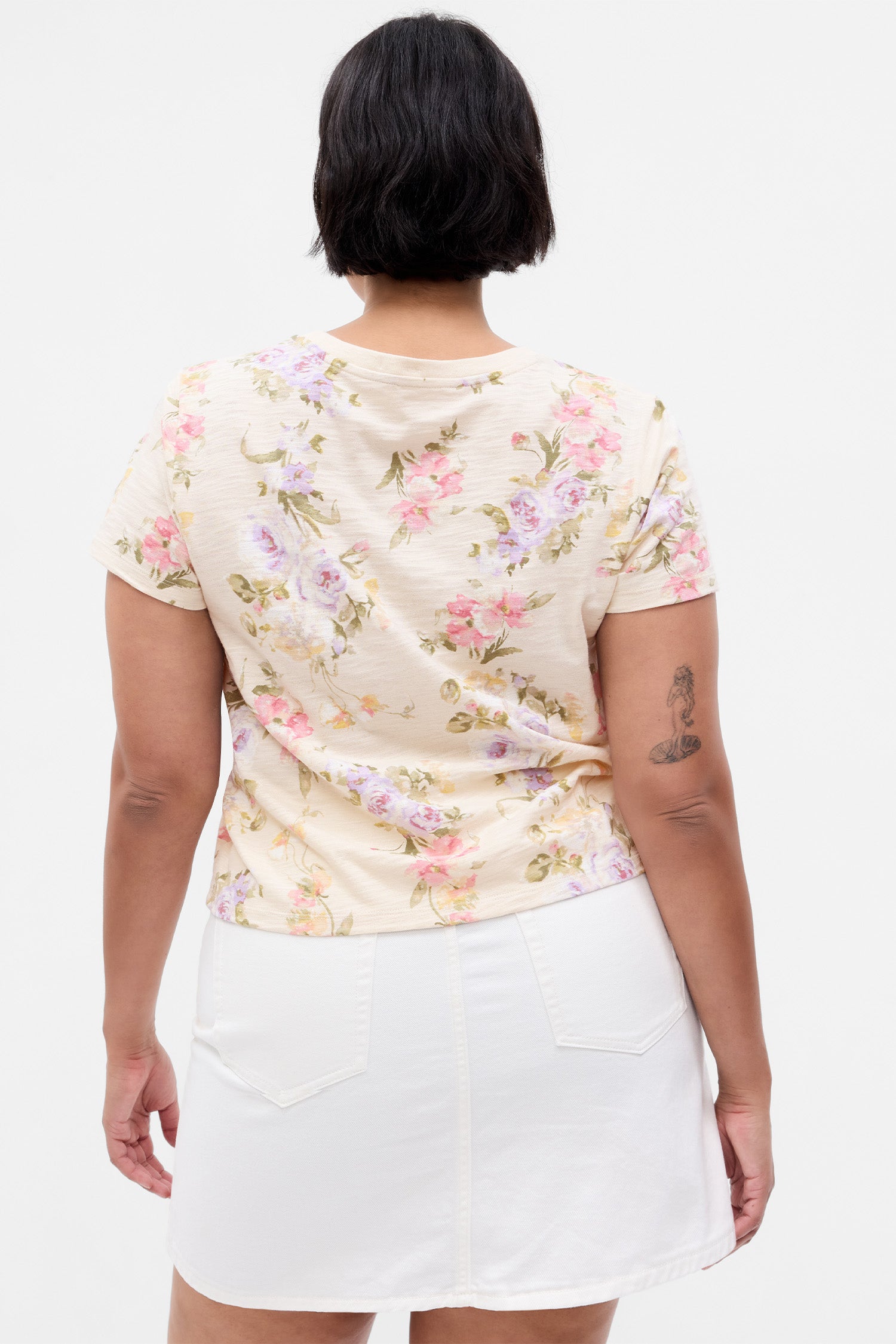 Back image of model wearing cream floral t-shirt with pink, purple, yellow, and green floral print