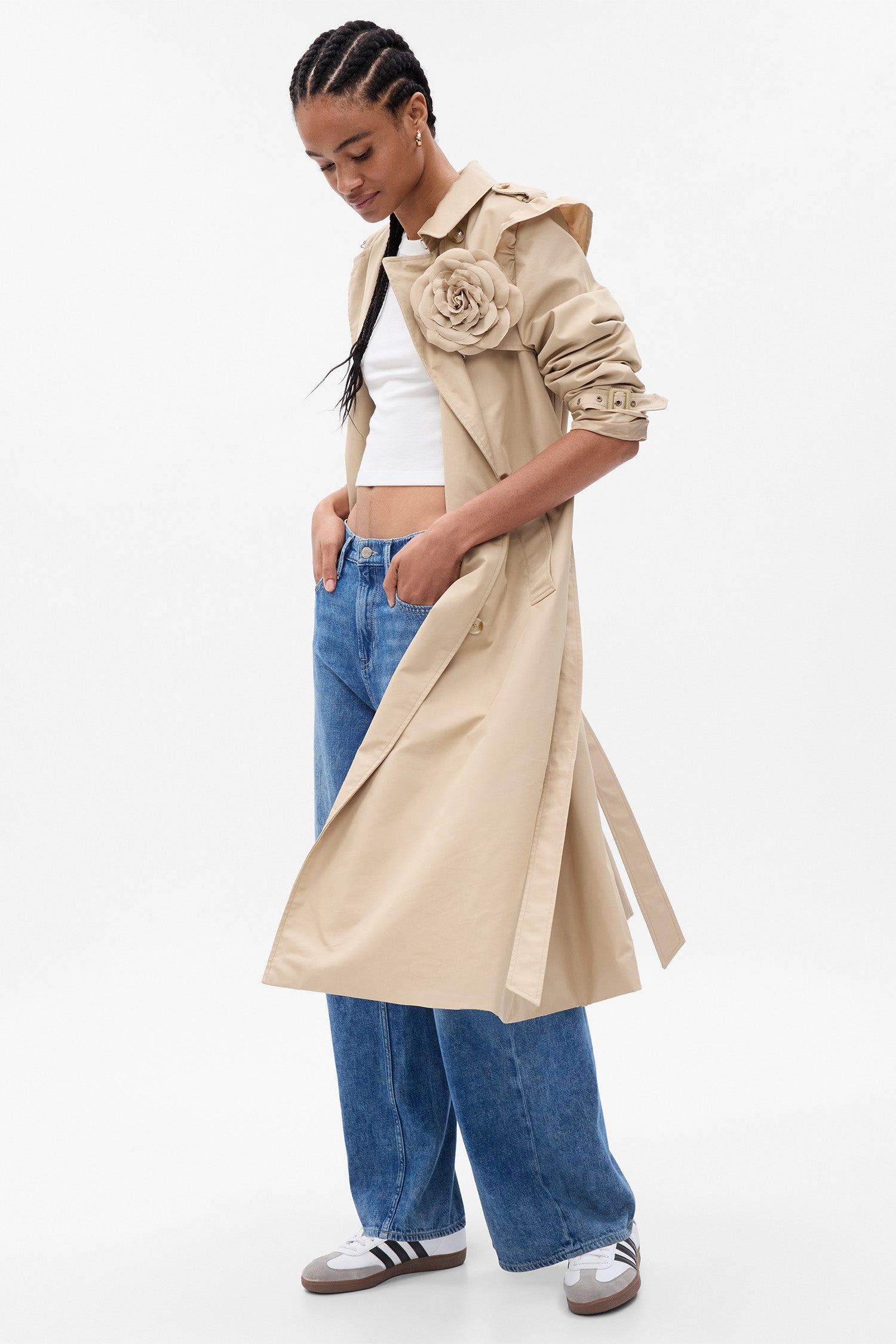 Model wearing khaki trench coat with rosette detail at chest