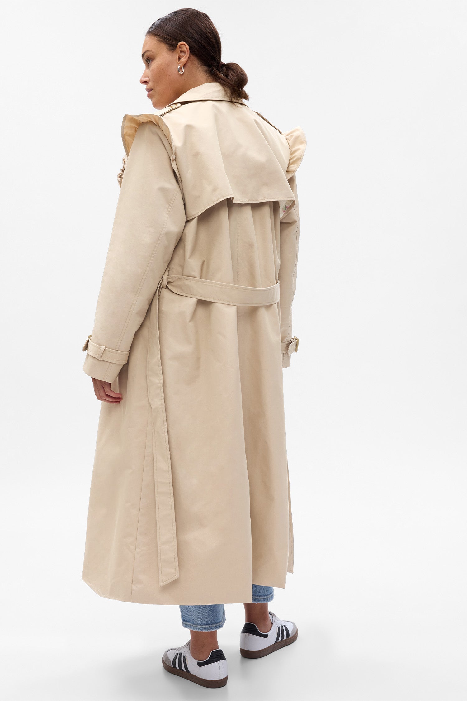Back image showing model wearing khaki trench coat with waist tie and ruffle shoulders