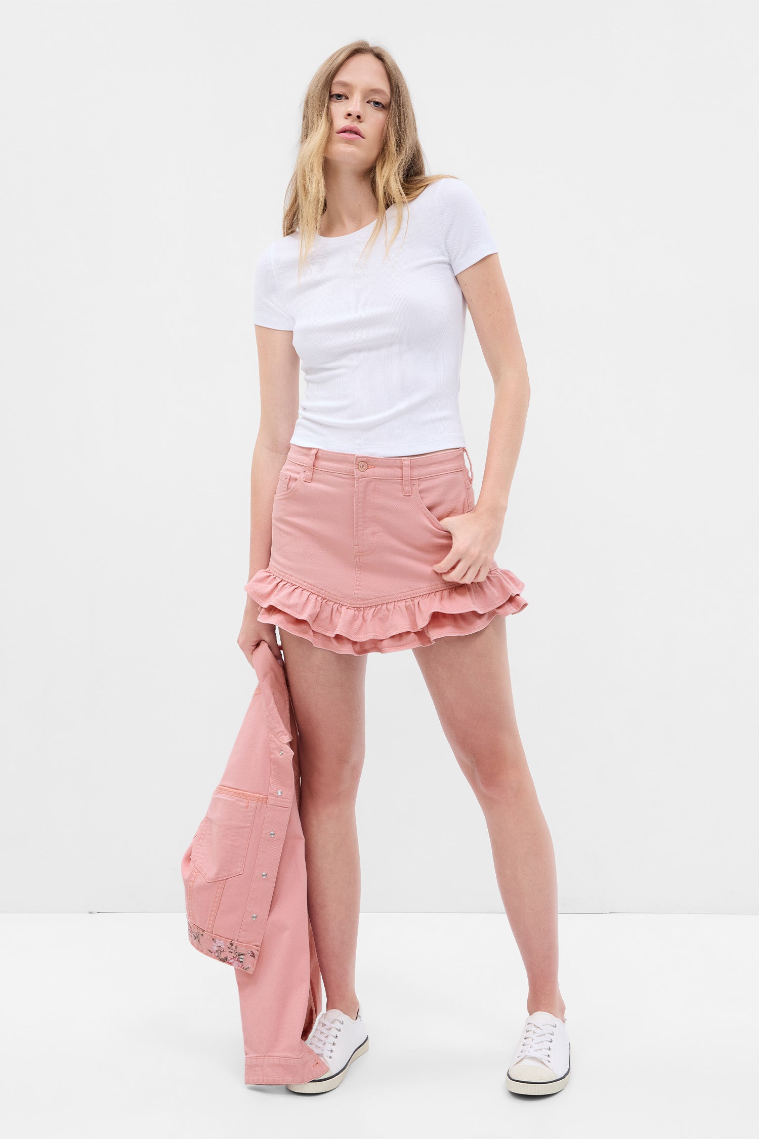 Model wearing pink denim mini skirt with ruffle detail at hem