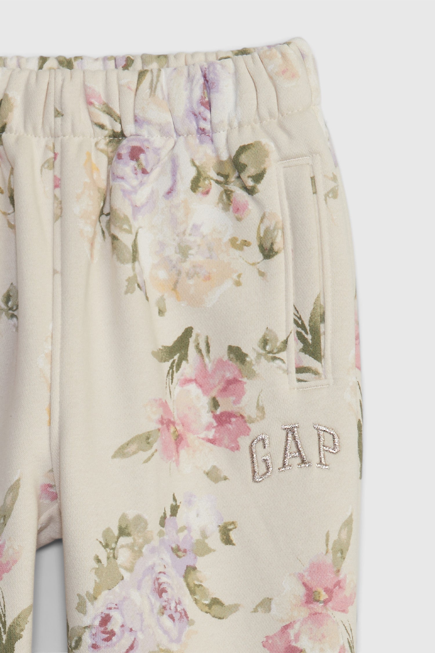 Close up image detailing GAP logo and pink, purple, yellow, and green floral print on girl's toddler cream joggers