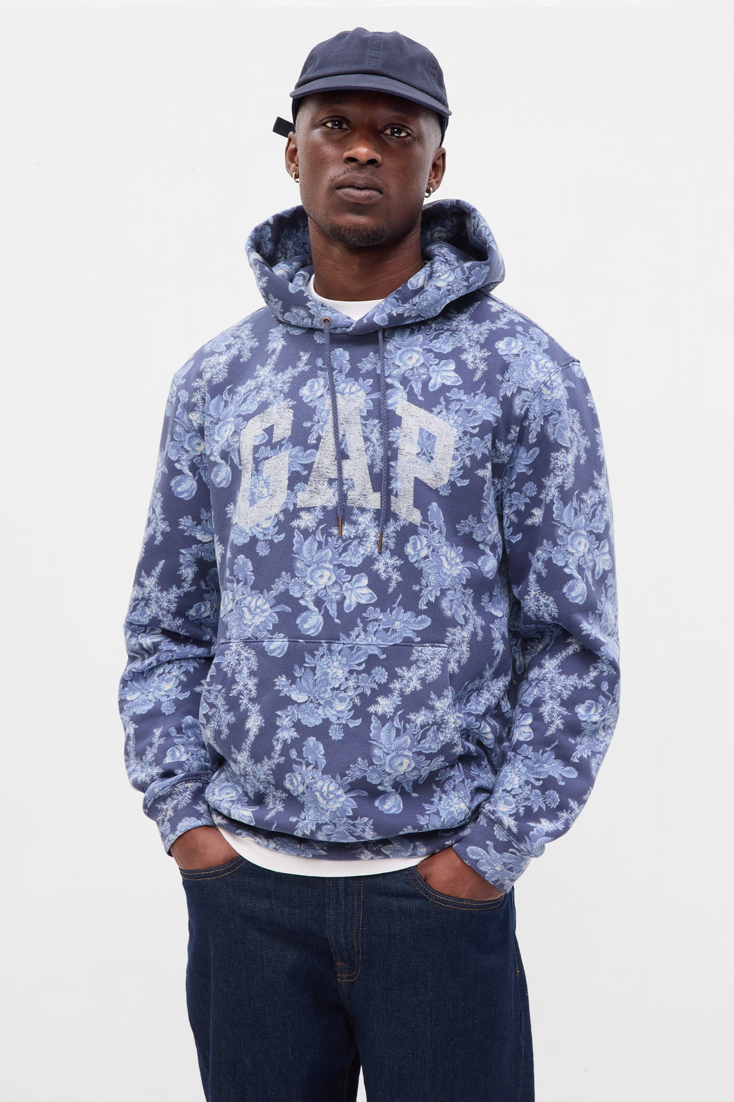 Model wearing men's blue floral hoodie with GAP logo at chest and front pocket. 