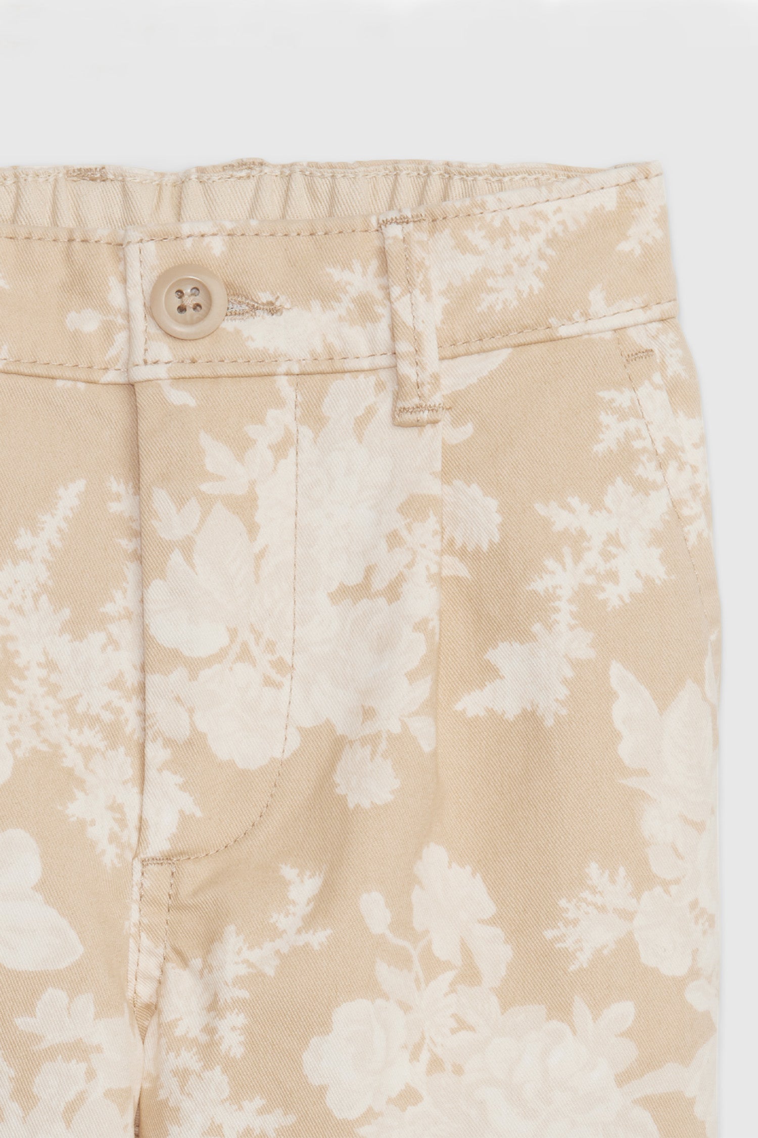 Close up image detailing floral print and button closure on boy's toddler cream floral khakis. 