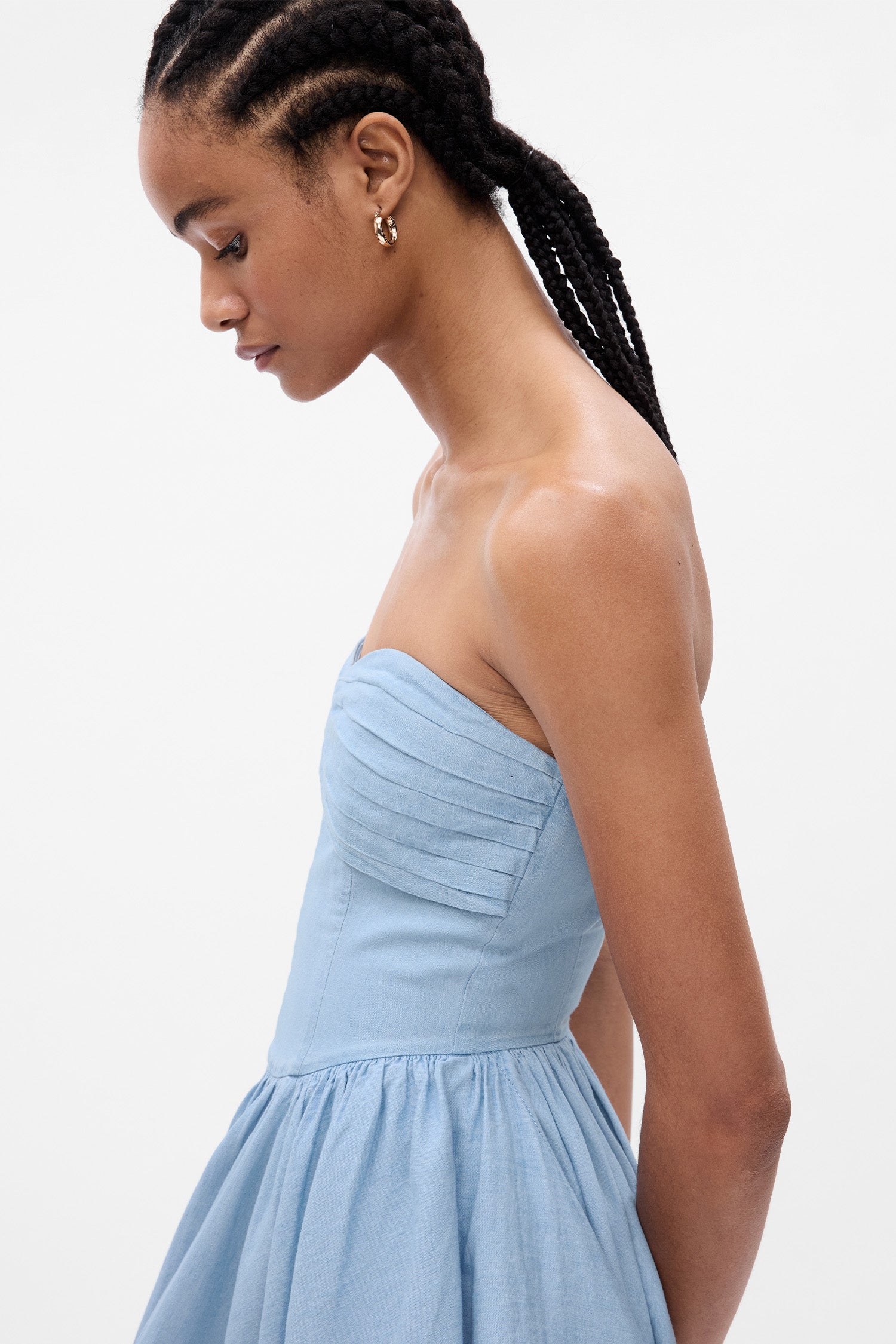 Close up image of model wearing blue denim strapless maxi dress with corset top and tiered skirt